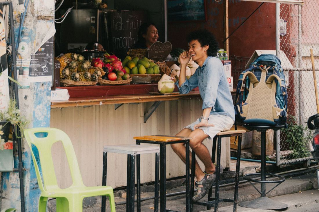A backpacker sitting and talking with the vendor at a street fruit stall in Chiang Mai